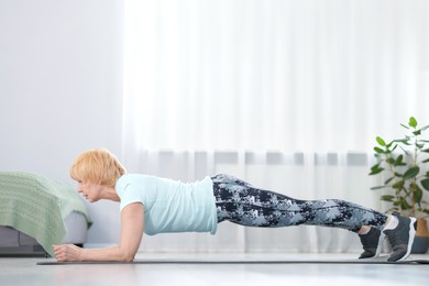 Photo of Senior woman in sportswear doing plank exercise at home