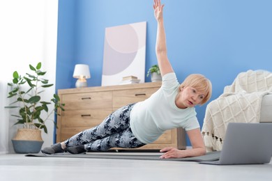 Photo of Senior woman in sportswear doing plank exercise during online class with coach at home