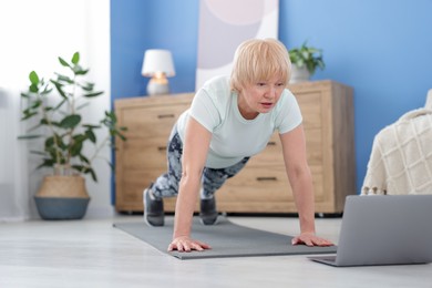 Photo of Senior woman in sportswear doing plank exercise during online class at home