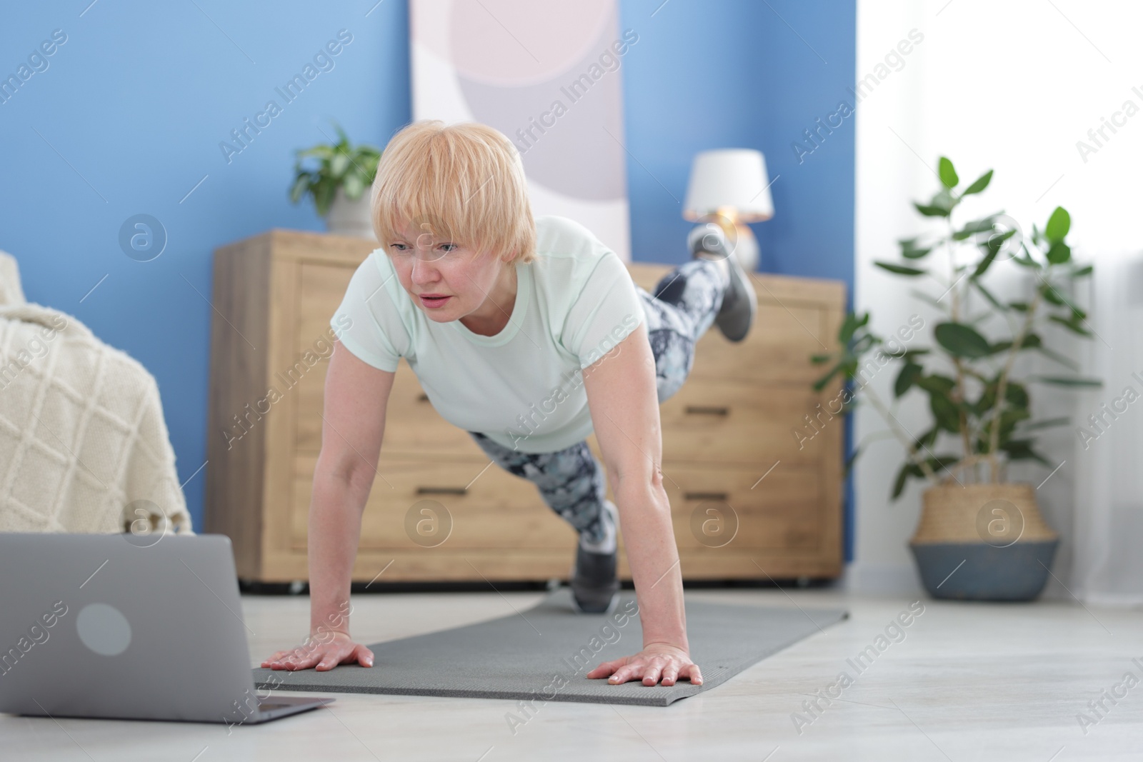 Senior woman in sportswear doing plank exercise during online class at home Photo of Senior woman in sportswear doing plank exercise during online class at home