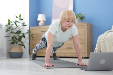 Photo of Senior woman in sportswear doing plank exercise during online class at home