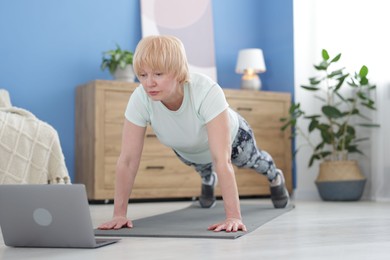 Photo of Senior woman in sportswear doing plank exercise during online class at home