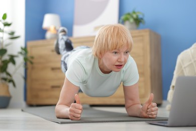 Photo of Senior woman in sportswear doing plank exercise during online class with coach at home