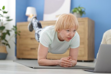Photo of Senior woman in sportswear doing plank exercise during online class with coach at home