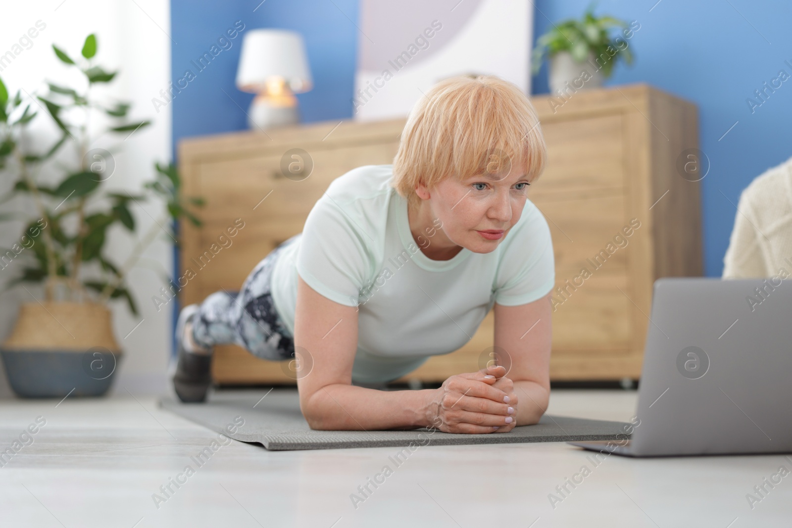 Senior woman in sportswear doing plank exercise during online class with coach at home Photo of Senior woman in sportswear doing plank exercise during online class with coach at home