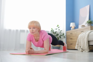 Photo of Senior woman in sportswear doing plank exercise at home