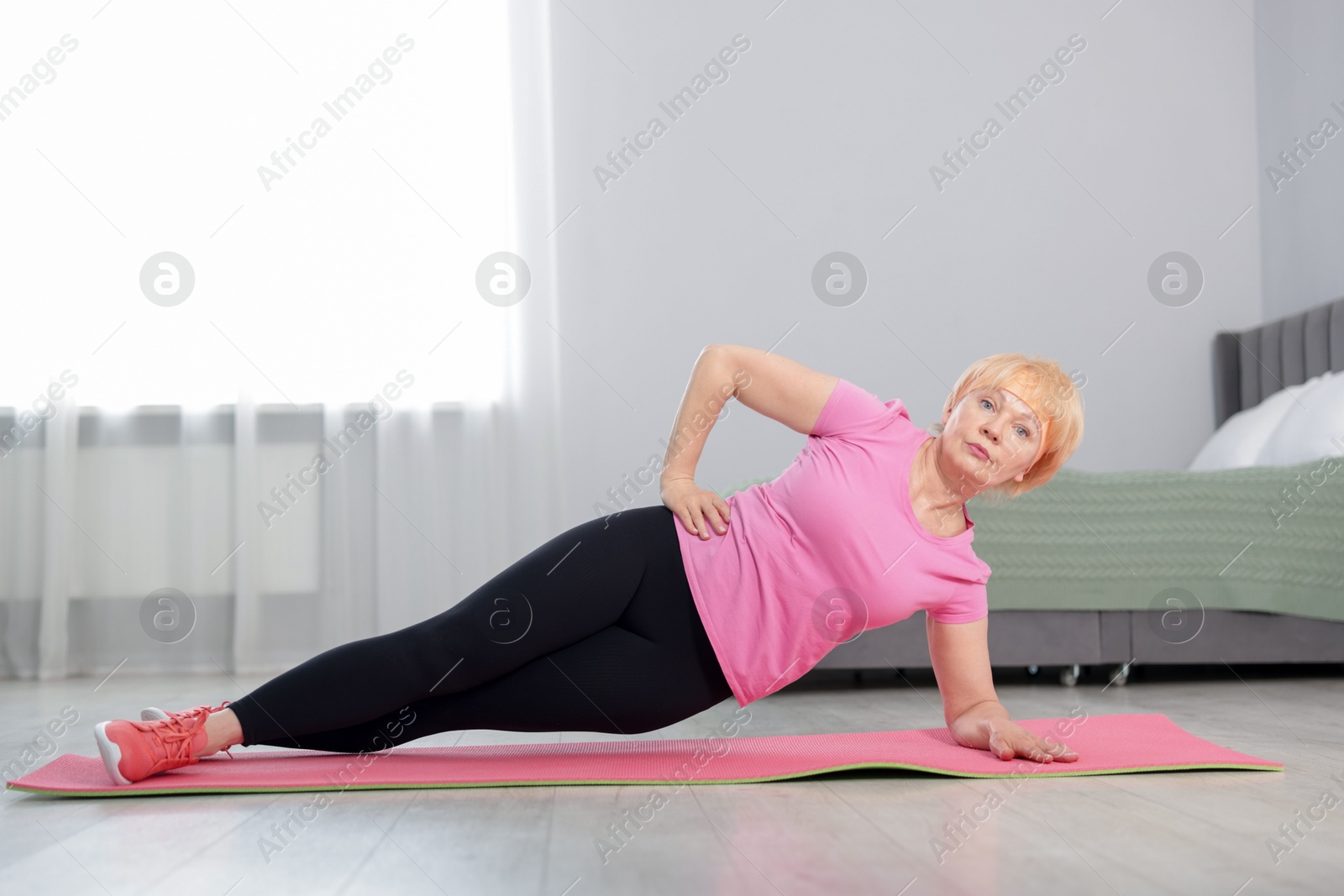 Photo of Senior woman in sportswear doing plank exercise at home