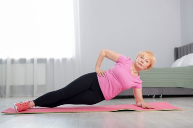 Photo of Senior woman in sportswear doing plank exercise at home