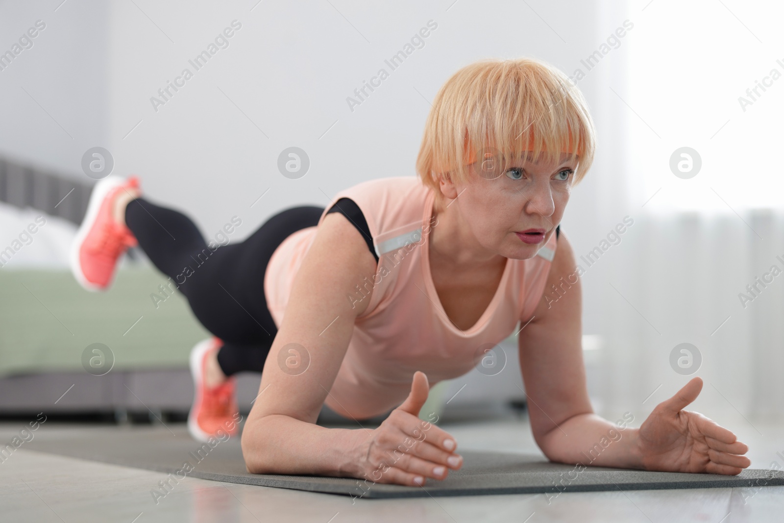 Photo of Senior woman in sportswear doing plank exercise at home