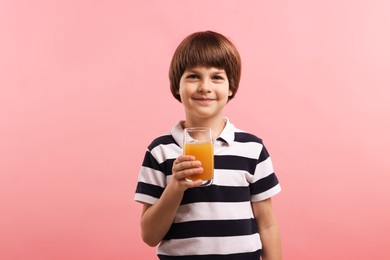 Photo of Cute little boy with glass of orange juice on pink background. Refreshing drink
