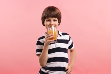 Photo of Cute little boy drinking orange juice on pink background. Refreshing drink