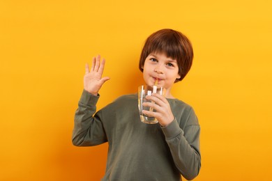Photo of Cute little boy drinking refreshing soda on orange background