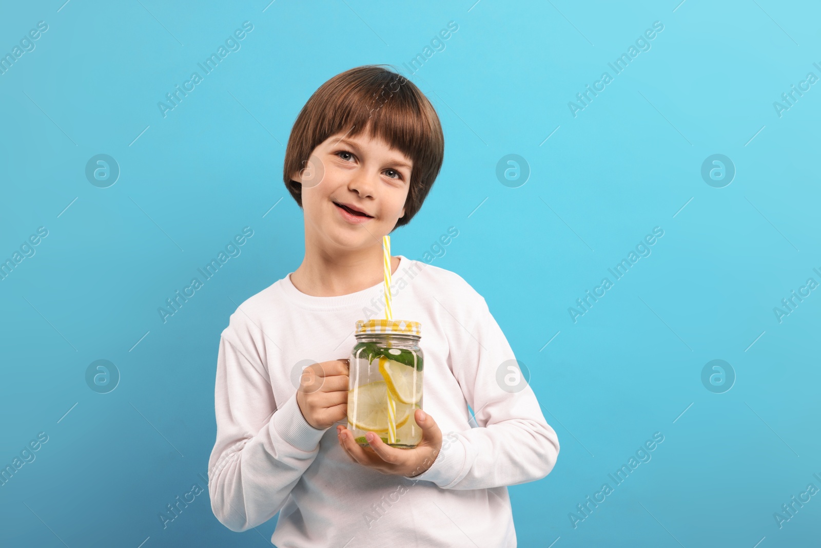 Cute little boy with mason jar of lemonade on light blue background. Refreshing drink Photo of Cute little boy with mason jar of lemonade on light blue background. Refreshing drink