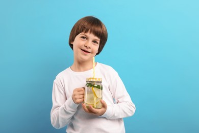 Photo of Cute little boy with mason jar of lemonade on light blue background. Refreshing drink