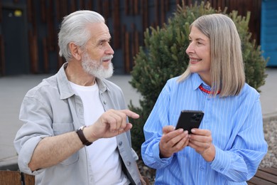 Photo of Lovely senior couple with smartphone on bench outdoors