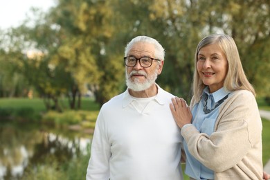 Photo of Lovely senior couple walking together near lake in park, space for text