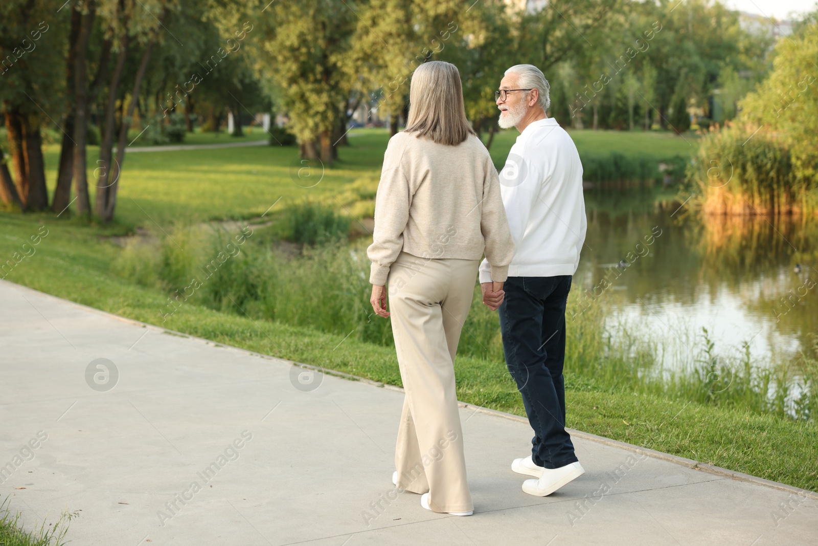 Lovely senior couple walking together near lake in park, space for text Photo of Lovely senior couple walking together near lake in park, space for text