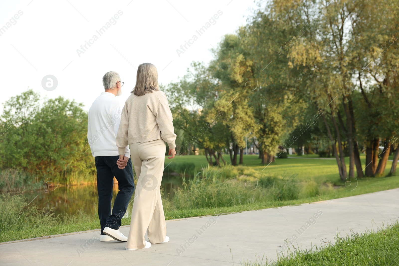 Lovely senior couple walking together near lake in park, space for text Photo of Lovely senior couple walking together near lake in park, space for text
