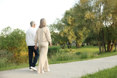 Photo of Lovely senior couple walking together near lake in park, space for text