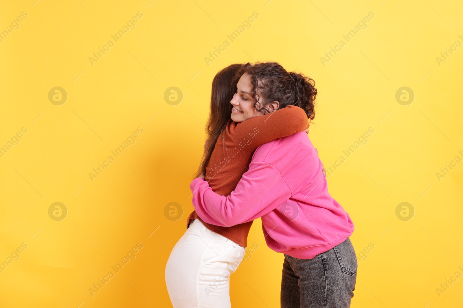 Friends hugging each other on orange background, space for text Photo of Friends hugging each other on orange background, space for text