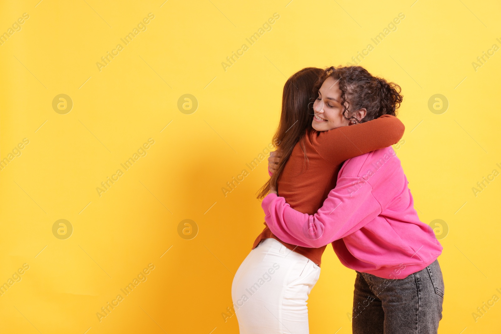 Friends hugging each other on orange background, space for text Photo of Friends hugging each other on orange background, space for text