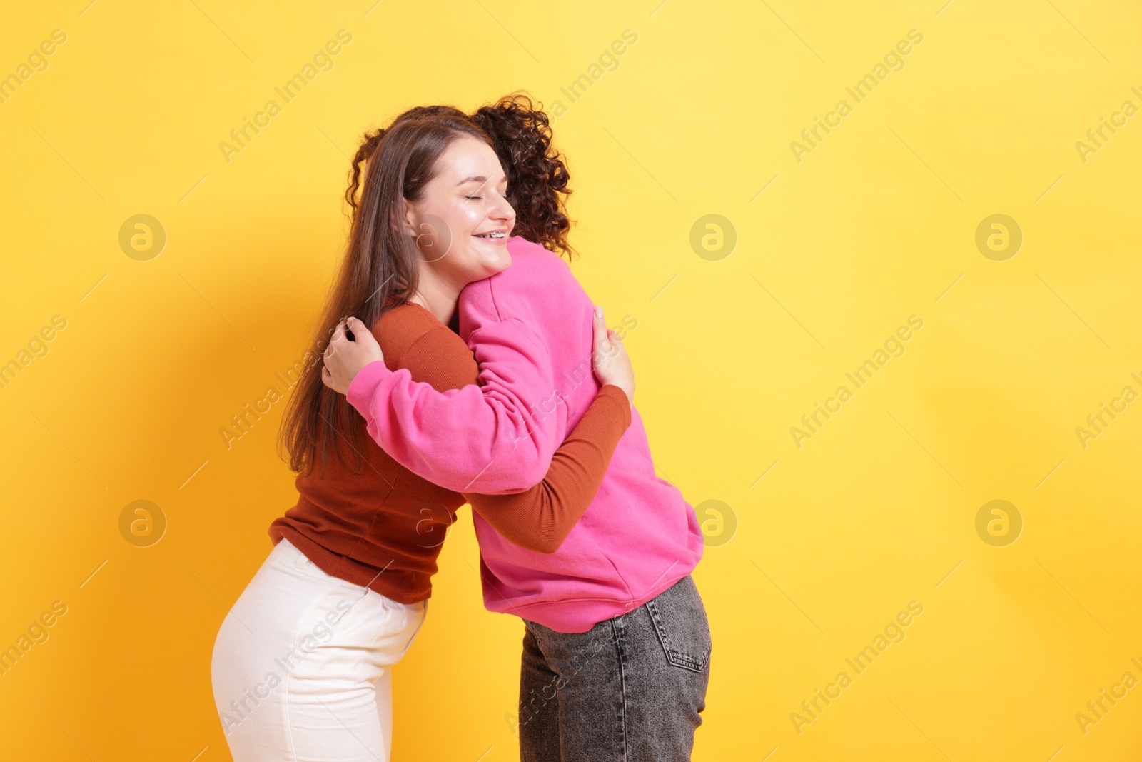 Friends hugging each other on orange background, space for text Photo of Friends hugging each other on orange background, space for text