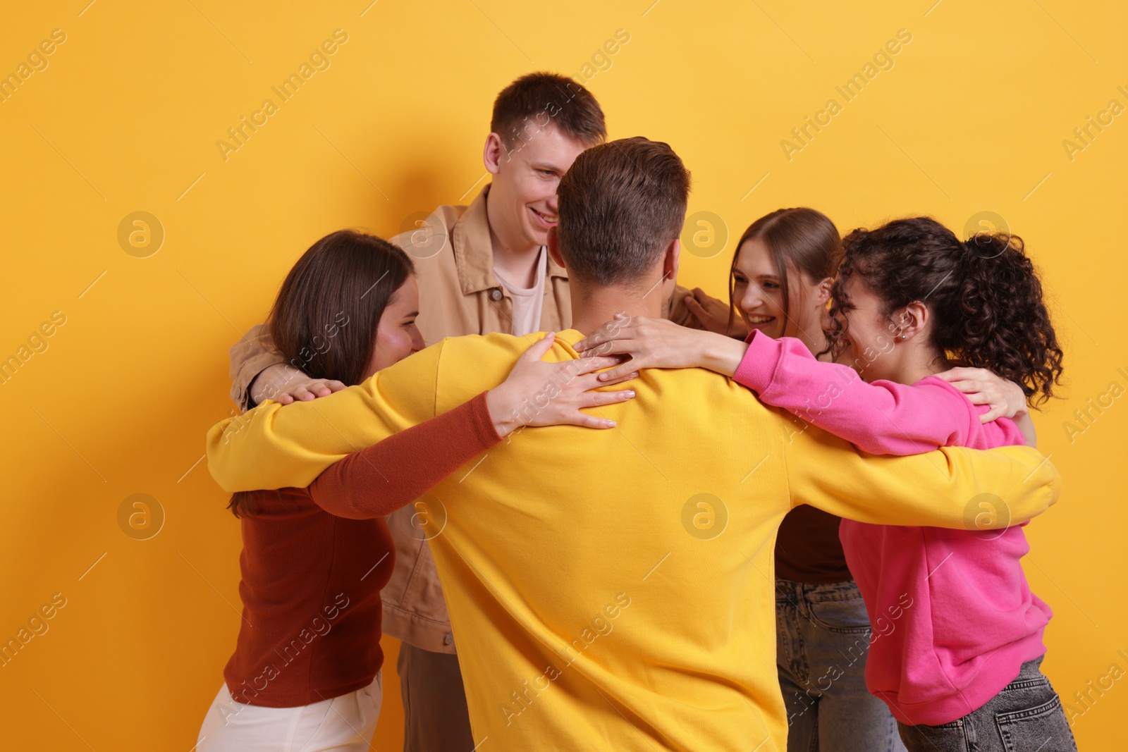 Group of friends hugging each other on orange background Photo of Group of friends hugging each other on orange background