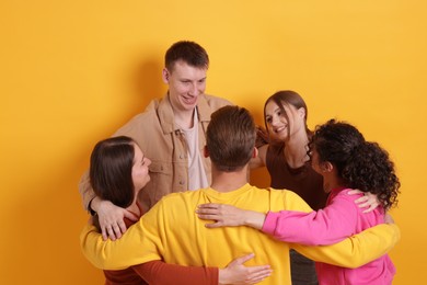 Photo of Group of friends hugging each other on orange background