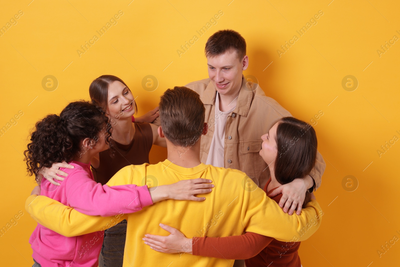 Group of friends hugging each other on orange background Photo of Group of friends hugging each other on orange background