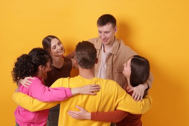 Photo of Group of friends hugging each other on orange background