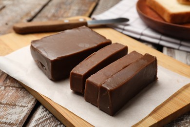 Photo of Pieces of tasty chocolate butter and knife on wooden table, closeup