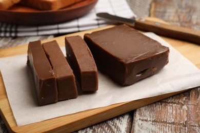 Photo of Pieces of tasty chocolate butter and knife on wooden table, closeup