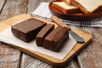 Photo of Tasty chocolate butter, slices of bread and knife on wooden table, closeup