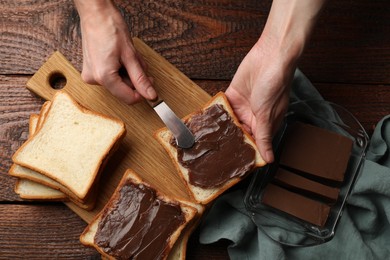 Photo of Woman spreading tasty chocolate butter onto bread at wooden table, top view