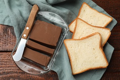 Photo of Tasty chocolate butter, slices of bread and knife on wooden table, flat lay