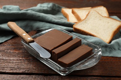 Photo of Tasty chocolate butter, slices of bread and knife on wooden table, closeup