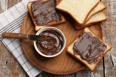Photo of Tasty chocolate butter, slices of bread and knife on wooden table, top view