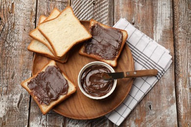 Photo of Tasty chocolate butter, slices of bread and knife on wooden table, top view