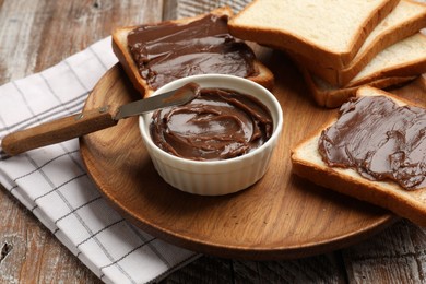Photo of Tasty chocolate butter, slices of bread and knife on wooden table, closeup