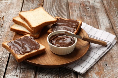 Photo of Tasty chocolate butter, slices of bread and knife on wooden table, closeup