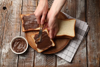 Photo of Woman spreading tasty chocolate butter onto bread at wooden table, top view