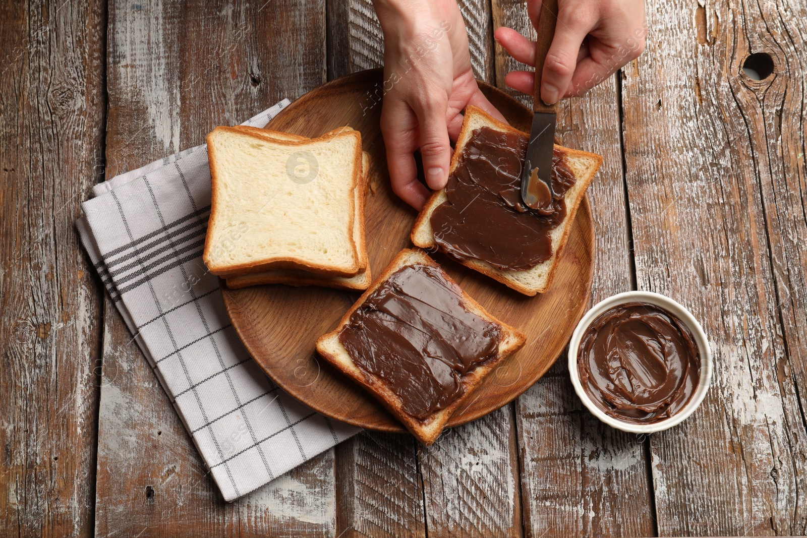 Woman spreading tasty chocolate butter onto bread at wooden table, top view Photo of Woman spreading tasty chocolate butter onto bread at wooden table, top view