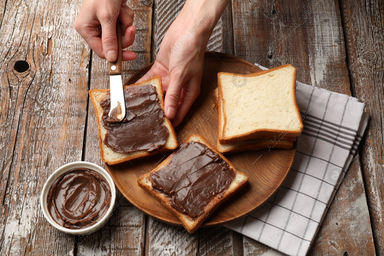 Woman spreading tasty chocolate butter onto bread at wooden table, above view Photo of Woman spreading tasty chocolate butter onto bread at wooden table, above view