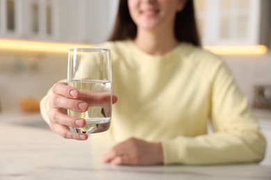 Photo of Woman with glass of water at table in kitchen, selective focus