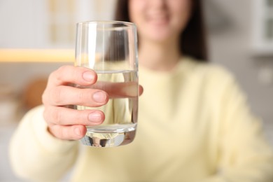 Photo of Woman drinking water from glass in kitchen, selective focus
