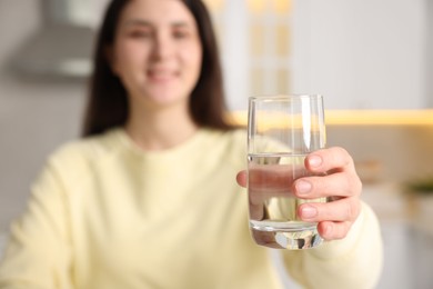 Photo of Woman drinking water from glass in kitchen, selective focus