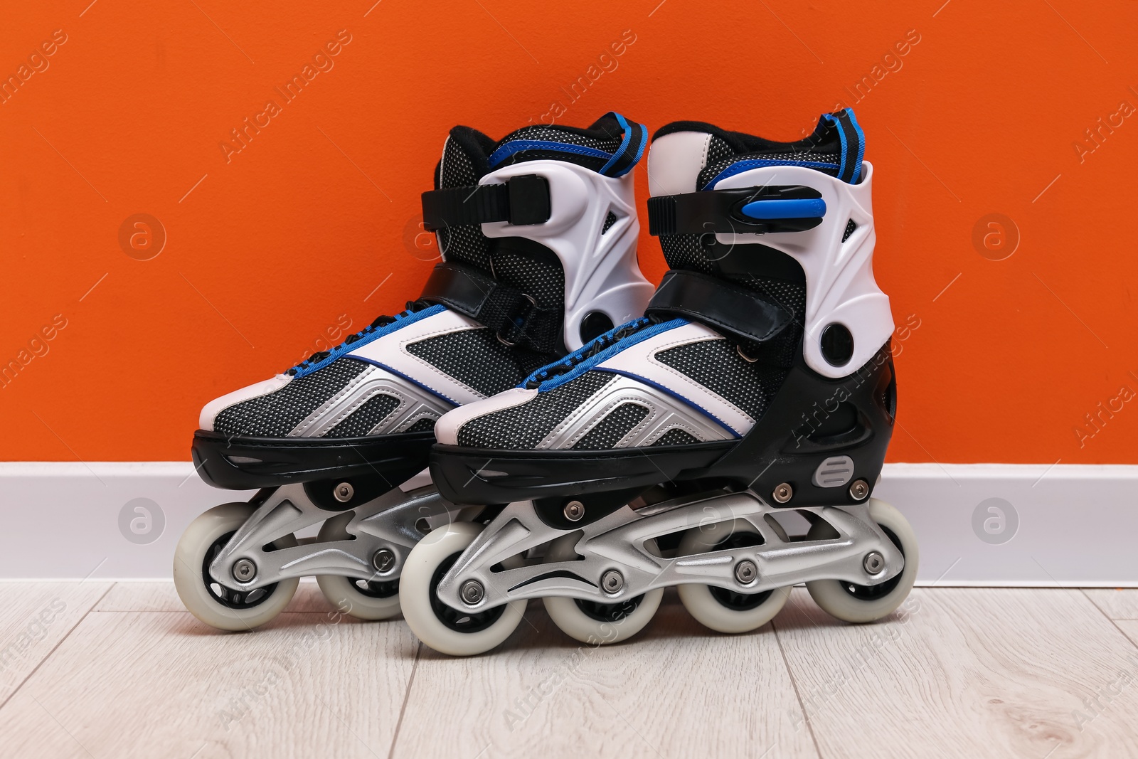 Pair of roller skates on floor near orange wall Photo of Pair of roller skates on floor near orange wall