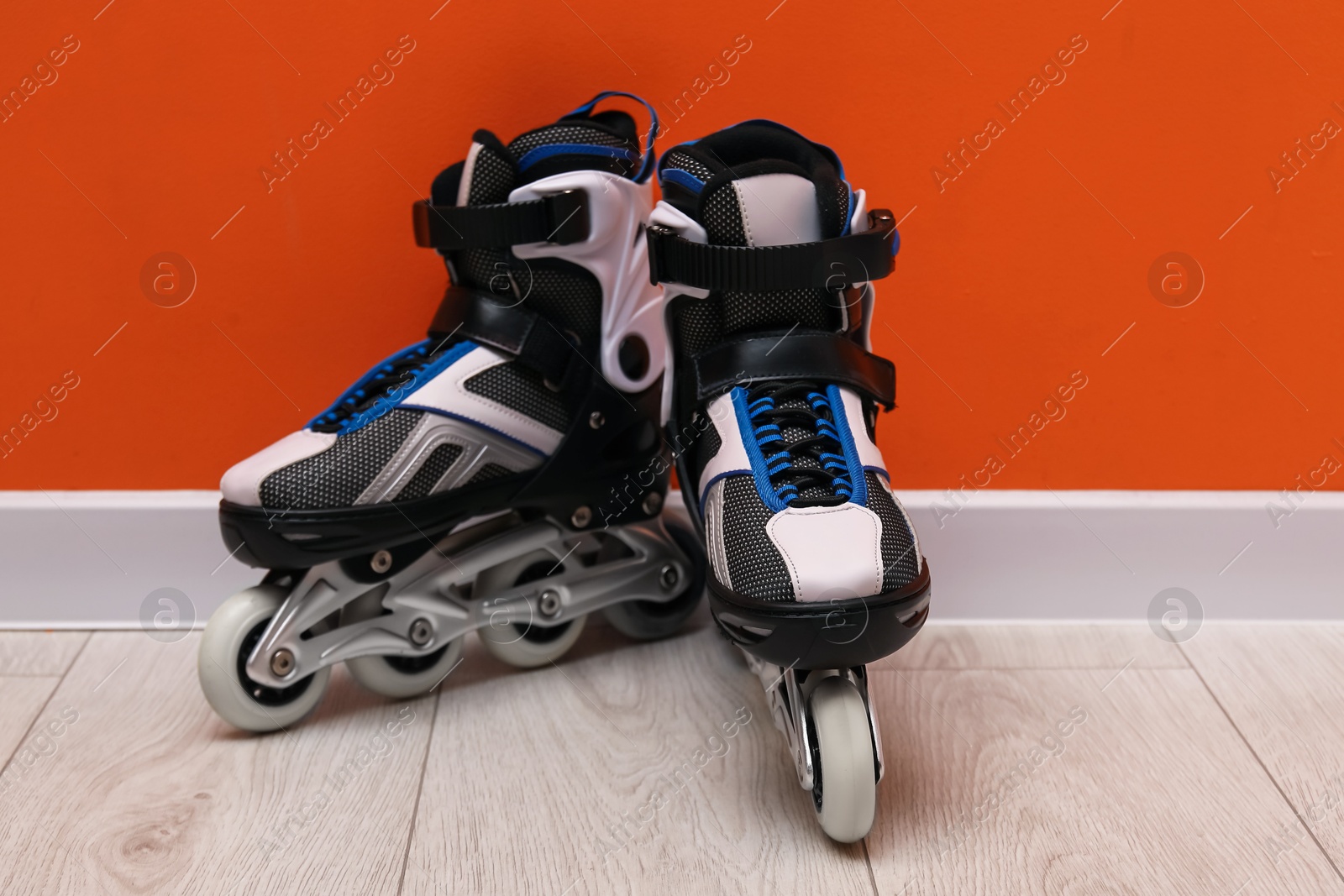 Pair of roller skates on floor near orange wall Photo of Pair of roller skates on floor near orange wall