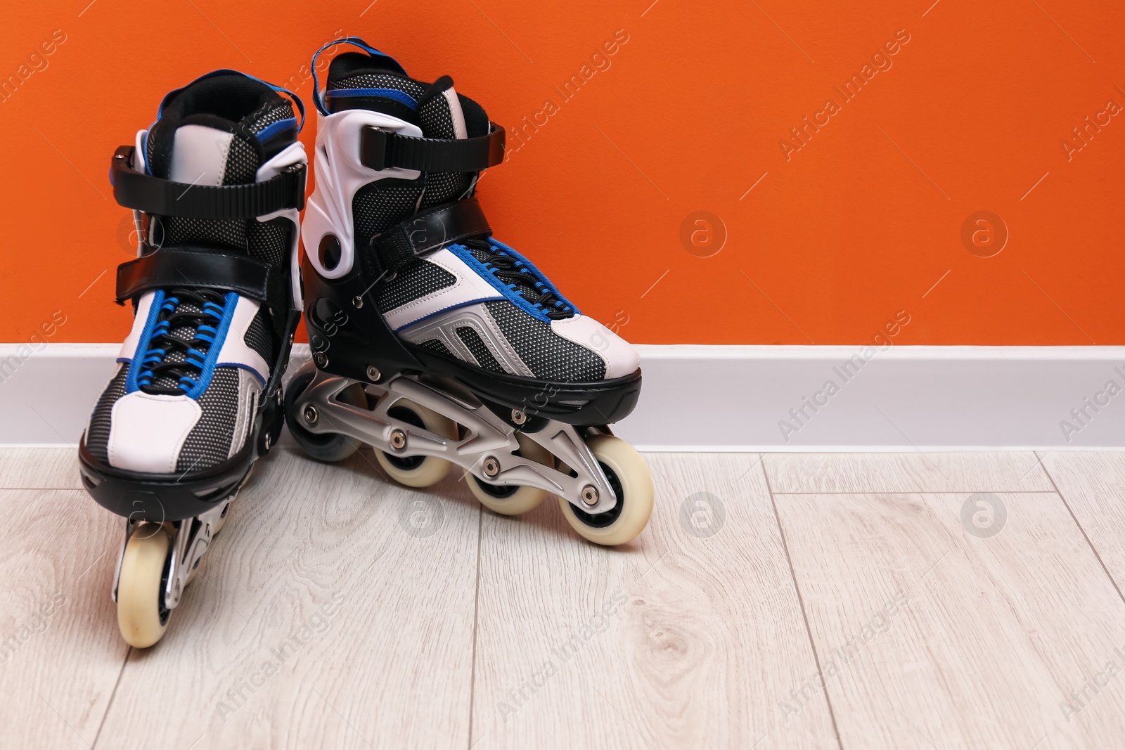 Pair of roller skates on floor near orange wall, space for text Photo of Pair of roller skates on floor near orange wall, space for text