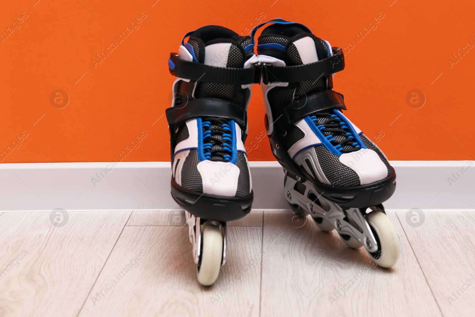 Pair of roller skates on floor near orange wall, space for text Photo of Pair of roller skates on floor near orange wall, space for text